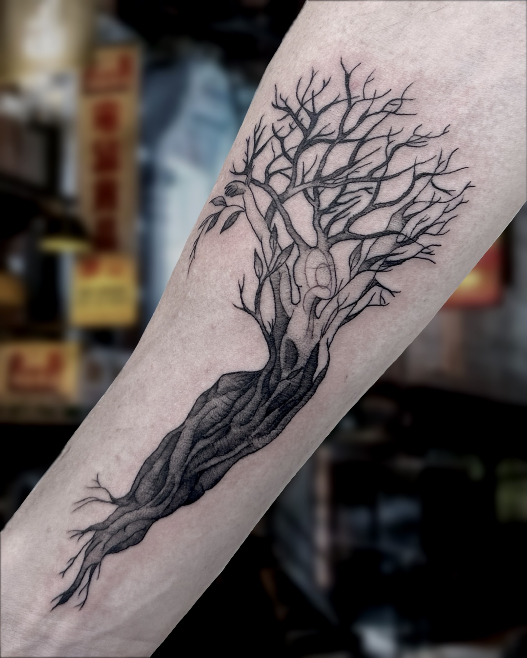 Black and grey bare tree with figure in trunk forearm tattoo