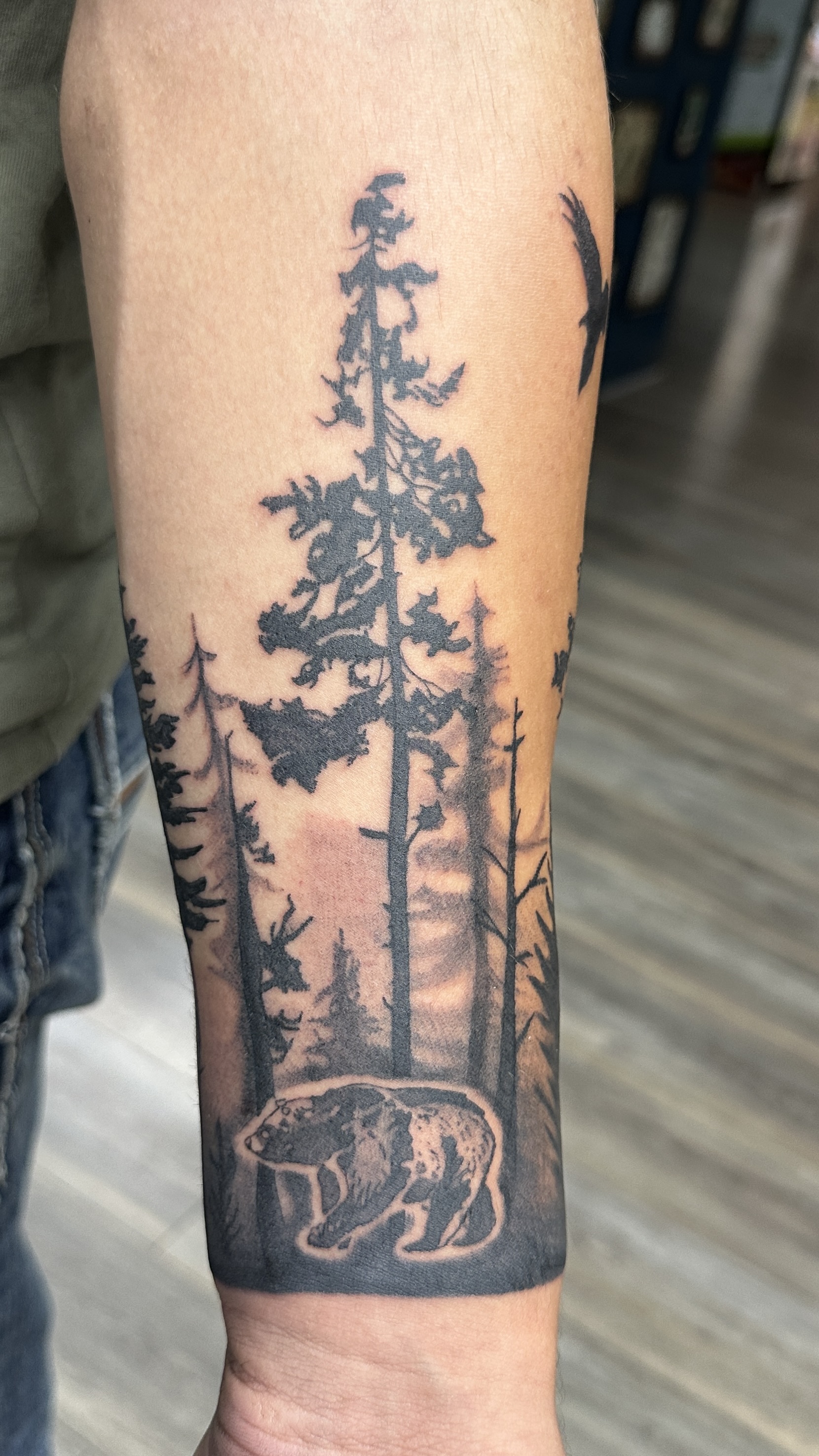 Black and grey pine forest with bear forearm tattoo